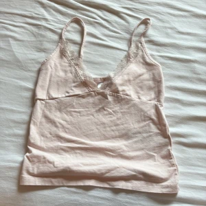 Ljusrosa linnetopp med spets Gina Tricot - Supersöt ljusrosa linnetopp från Gina Tricot med tunna axelband och v-ringning dekorerad med spets. Toppen är i mjuk bomull och har en feminin, enkel look som passar perfekt till jeans eller kjol. Perfekt för varma dagar eller lager på lager.                                                                                    Fåtal använd och har bra skick! 🌟