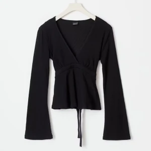 Svart omlottopp med knytband - Svart omlottopp med långa ärmar och v-ringning. Toppen har knytband i midjan och lätt utsvängda ärmar för en cool siluett. Perfekt att styla med jeans eller kjol för en trendig look.