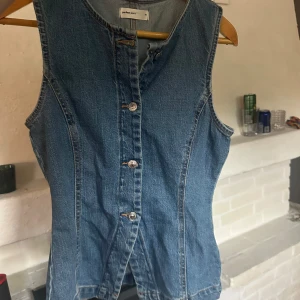 Jeansväst från Gina tricot - Snygg jeansväst i klassisk blå denim från Gina tricot. Västen är ärmlös, har figurnära passform.