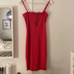 Röd ribbad klänning från Missguided - Röd ribbad klänning från Missguided med smala axelband och snygga knappar framtill. Modellen är kroppsnära och har en lätt volangkant upptill. Perfekt för dig som vill sticka ut med en färgstark look.
