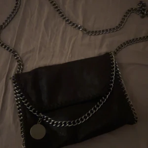 Svart axelväska med kedjedetaljer - Snygg svart axelväska med silverkedja som axelrem och runt kanterna. Väskan har ett lock och insidan är fodrad med leopardmönster. Det finns flera fack i väskan. 