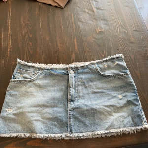 Mini jeanskjol  - Säljer en assnygg ljusblå mini jeanskjol från Pull&Bear. Kjolen är KORT med fransade kanter upptill och nedtill! Endast använd 1 gång 🥰 strl L men liten i storlek