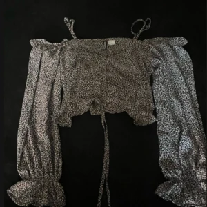 Blommig croppad blus från H&M Divided - Supersöt croppad blus med blommigt mönster i svart, vitt och ljusrosa. Långa puffärmar med resår och volang vid ärmslut, smala axelband och snörning framtill. Perfekt för dig som gillar romantisk och trendig stil.