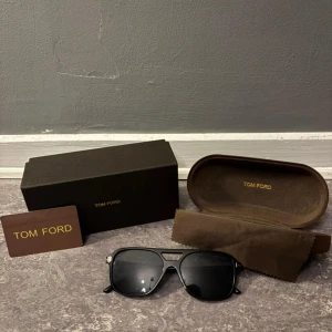 Tom Ford glasögon  - Snygga svarta solglasögon från Tom Ford i klassisk aviator-modell. Glasögonen har svarta bågar i plast med diskreta gulddetaljer vid gångjärnen och mörka linser. Kommer med originalfodral, putsduk och box. Perfekt accessoar för en cool look.