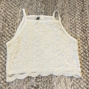 Vit spetsig croppad linnetopp Divided - Vit croppad linnetopp från Divided med spets och blommigt mönster. Toppen har tunna axelband och vågig kant nertill. Från H&M i storlek M, materialet är stretchigt, passar mindre storlekar också (brukar själv ha S)
