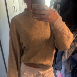 Beige stickad tröja med hög krage - Mysig beige stickad tröja med hög krage och långa ärmar. Tröjan har en loose passform och breda ribbade muddar vid ärmslut och nederkant. Perfekt för lager-på-lager och chill dagar.