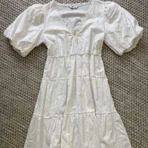 Vit klänning med broderade blommor - Superfin vit klänning från Cubus i bomull med broderade blommor och v-ringning. Puffiga korta ärmar och volangiga lager ger en romantisk vibe. Perfekt för sommarens alla tillfällen. Säljes i storlek XS.