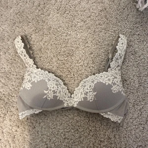 Grå spets-bh med vita detaljer - Superfin grå bh med vita spetsdetaljer längs kanterna och axelbanden. Bh:n har vadderade kupor och ett elegant mönster i tyget. pris kan diskuteras❤️