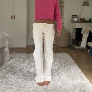 Vita jeans  - Säljer ett par vita super snygga jeans med låg midja och snygg snörning framtill. Byxorna har raka ben med lätt utsvängd passform. Perfekta för dig som vill ha en cool och trendig look.