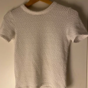 Vit stickad topp från Bershka - Säljer en vit topp från Bershka i storlek S. Toppen har korta ärmar och är gjord i ett strukturerat, stickat material som ger en cool textur. Enkel och stilren design med rund halsringning💐🥂❤️