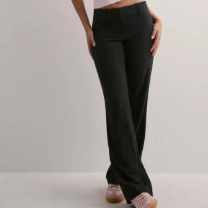 Svarta kostymbyxor  - ”Super Low Waist Flare Suit Pant” från Nelly. Byxorna har bälteshällor och klassisk stängning framtill. Perfekta för en clean och stilren look. Materialet är mjukt och följsamt, vilket gör dem riktigt bekväma. Aldrig använda 