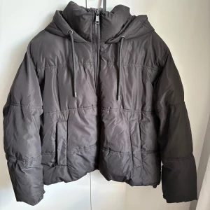 Zara svart pufferjacka med huva och dragkedja - Säljer en svart pufferjacka med huva och dragsko från Zara. Jackan har dragkedja framtill, två fickor och en oversized passform. Pris kan diskuteras. Används ett antal gånger, men är i mycket bra skick. Water resistant.