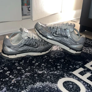 Nike P-6000 silver sneakers - Nike P-6000 sneakers i metallic silver och grå med svart swoosh. Ovandel i mesh och syntet med coola paneler och vita snören. Snygg retrovibe och chunky sula i vitt och svart. Perfekta för dig som vill sticka ut med futuristisk stil. Sjukt populära skor sjukt bekväma passar till mycket! Säljer då jag har för många skor 