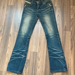 Blå bootcut jeans med broderade detaljer - Snygga blå jeans med broderade detaljer på bakfickorna och en cool slitningseffekt. Byxorna har en bootcut-stil och är perfekta för en avslappnad look. De har också knappar och dragkedja framtill.