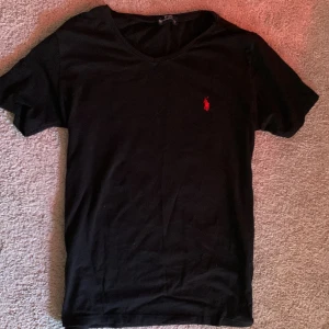 Svart t-shirt från Polo Ralph Lauren - Snygg svart t-shirt från Polo Ralph Lauren med en   v-ringad hals och korta ärmar, perfekt för en stilren look.