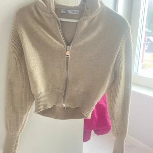 Beige stickad hoodie från Zara - Säljer en beige stickad hoodie från Zara med dragkedja framtill. Tröjan är croppad och har långa ärmar samt en mysig huva. Perfekt för en avslappnad stil.