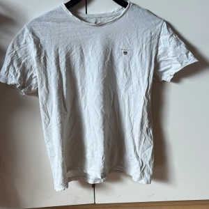 Vit t-shirt från GANT - Säljer en klassisk vit t-shirt från GANT med en liten broderad logga på bröstet. T-shirten är kortärmad och tillverkad i mjuk bomull. Perfekt för en avslappnad stil.