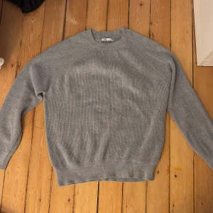 Grå stickad tröja från Zara - Säljer en stilren grå stickad tröja från Zara. Perfekt för kyligare dagar med sin mjuka och bekväma passform. Tröjan har långa ärmar och en rund halsringning. Passar utmärkt till både jeans och chinos.