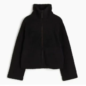 Svart teddyjacka  - Mysig svart teddyjacka med dragkedja framtill. Jackan har en hög krage och långa ärmar, perfekt för kyligare dagar. Den har en enkel och stilren design som passar till många olika outfits.