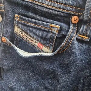 Mörkblå jeans från Diesel - Snygga mörkblå jeans från Diesel med klassisk femficksdesign och kontrastsömmar. Perfekta för en stilren look. Märkesdetaljer på fickan och insidan av linningen.
