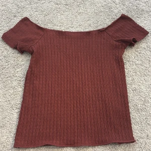 Vinröd ribbad offshoulder topp - Säljer en snygg vinröd ribbad offshoulder topp. Perfekt för en avslappnad stil med korta ärmar och en bekväm passform. Passar bra till både jeans och kjol. Hör av dig vid intresse! Litet hål på baksidan men inget som märks
