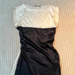 Svart och vit klänning - Snygg svart och vit klänning med en elegant design. Klänningen har en kontrasterande färgblocksstil med en vit överdel och svart nederdel. Perfekt för en stilren look.