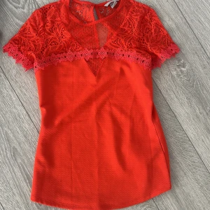 Röd spetsblus från H&M - Snygg röd blus från H&M med spetsdetaljer och korta ärmar. Perfekt för en färgglad look. Blusen har en rund hals och en liten öppning bak i nacken.
