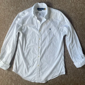 Vit skjorta från Ralph Lauren - Säljer en klassisk vit skjorta från Ralph Lauren i slim fit. Skjortan är långärmad och har en broderad logotyp på bröstet. Tillverkad i 100% bomull med stretch för extra komfort. Perfekt för en stilren look.