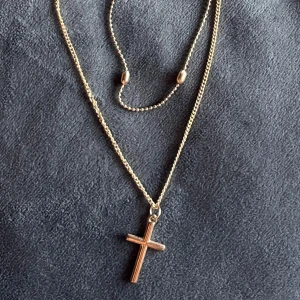 Guldhalsband med korshänge - Elegant guldhalsband med ett korshänge. Halsbandet har en dubbel kedja med små dekorativa pärlor och ett justerbart lås för perfekt passform.