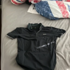 Svart pikétröja från BOSS - Snygg svart pikétröja från BOSS med gröna detaljer. Tröjan har en klassisk krage och korta ärmar. Perfekt för en stilren look.