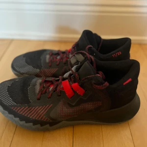 Svarta och röda sneakers från Nike -  Kyrie Irving! Mycket bra skick! Snygga svarta sneakers med röda detaljer från Nike. Skorna har en robust sula med mönster för bra grepp och snörning för justerbar passform. Perfekta för både träning och vardag.