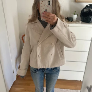 Beige kappa Bubbleroom - Säljer en stilren beige kappa från Bubbleroom. Den har en dubbelknäppt design med stora knappar och en klassisk krage. Perfekt nu till våren!💕 Inte använd mycket så i bra skick. Köpte för 600kr men säljer för 300kr!☺️