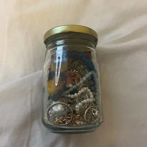  Mystery jar  - En glasburk fylld med olika smycken och accessoarer. Innehåller bland annat pärlhalsband, guldfärgade kedjor och hårklämmor. Perfekt för den som vill ha en mix av stilar och material.