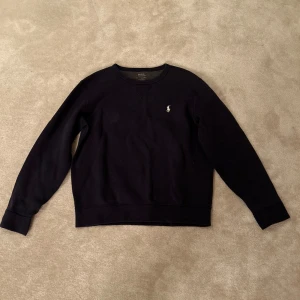 Svart tröja från Polo Ralph Lauren - Snygg marinblå tröja från Polo Ralph Lauren med klassisk logga på bröstet. Tröjan har långa ärmar och en rund halsringning. Perfekt för en stilren look. Storlek 170. Använt ganska mycket så rätt så urtvättad men fortfarande skön och ha på sig. 