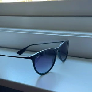 Svarta solglasögon från Ray-Ban - Snygga svarta solglasögon från Ray-Ban med en klassisk rund form. De har tunna skalmar och mörka glas som ger ett stilrent intryck. Perfekta för soliga dagar och en tidlös accessoar i garderoben.