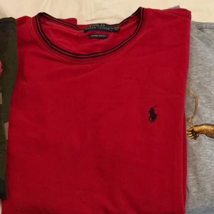 Röd tröja från Ralph Lauren - Säljer en snygg röd tröja från Ralph Lauren med det klassiska logotypbroderiet på bröstet. Tröjan har en rund halsringning med svarta detaljer och är i en custom slim fit passform.