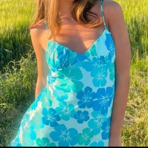 Blommig klänning med smala axelband - Snygg klänning med blommigt mönster i blå och turkosa nyanser. Den har smala axelband och en v-ringad design som ger en somrig känsla.