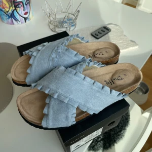 HELT NYA Ljusblå sandaler från Duffy - Helt nya, original packning. Snygga ljusblå sandaler från Duffy med volangdetaljer. Korsade remmar i textilmaterial. 