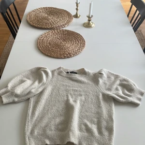 Beige stickad tröja Vero Moda puffärm - Superfin beige stickad tröja från Vero Moda med puffärmar och ribbade muddar. Tröjan har en klassisk rund halsringning och är perfekt för dig som gillar en stilren men trendig look. Passar lika bra till jeans som till kjol.
