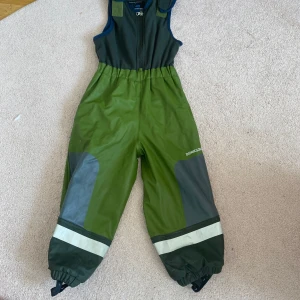 Gröna täckbyxor från Didriksons - Säljer gröna täckbyxor från Didriksons med reflexdetaljer och förstärkta knän. Byxorna har dragkedja framtill, elastiska benslut och justerbara axelband. Perfekta för utomhuslek under kalla och blöta dagar.