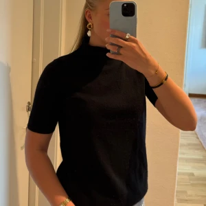 Svart polotröja i kashmir från Soft Goat - Svart polotröja i 100% kashmir från Soft Goat. Tröjan har korta ärmar, hög krage och en klassisk, stilren look. Perfekt till jeans eller kjol för en clean vibe. Mjuk och lyxig känsla, passar dig som gillar minimalistiskt mode.🌟