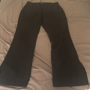 Svarta bootcut kostymbyxor - Snygga svarta kostymbyxor från Vero Moda med bootcut passform och midwaist/låg midja. Byxorna har en klassisk och tidlös design med vida ben och diskreta slitsar nedtill för en stilren look. Perfekta till både vardag och fest! Använda ett fåtal gånger – i mycket fint skick. Nypris ca 400 kr. 💌 Köparen står för frakten. 