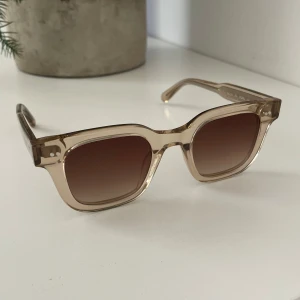 Beige solglasögon från Chimi - Snygga solglasögon från Chimi i modellen 04 Ecru. Glasögonen har en fyrkantig form med transparent beige båge och bruna tonade glas. Perfekta för att ge en trendig touch till din stil.