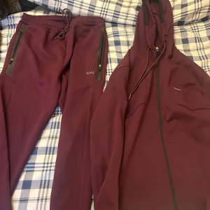 Vinröda Tracksuit från BOSS - Vinröd Hugo Boss komplett tracksuit. Perfekta för chill eller träning, med en modern och sportig look. Mjukt material och diskret logga på benet.