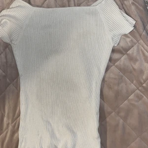 Vit ribbad topp från H&M - Säljer en vit ribbad topp från H&M i storlek M. Toppen har korta ärmar och är figurnära med stretchigt material. Perfekt för att styla med jeans eller kjol för en clean look. Enkel och stilren design med rund halsringning.