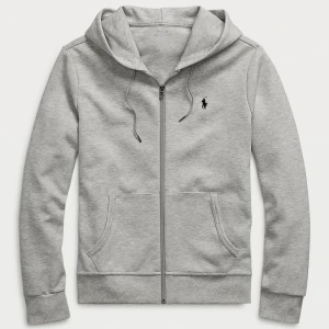 Grå hoodie från Polo Ralph Lauren - Snygg grå hoodie från Polo Ralph Lauren med dragkedja och huva. Klassisk logga broderad på bröstet, snörning i huvan och två fickor framtill. Perfekt för en chill och stilren look.