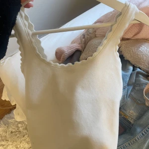 Vit ribbad linnetopp med vågig kant Zara - Supersöt vit linnetopp med vågig kant runt halsringningen och ärmhålen. Toppen är ärmlös och har en enkel, clean look som passar perfekt till jeans eller kjol. Materialet känns mjukt och stretchigt, vilket gör den riktigt skön att bära.