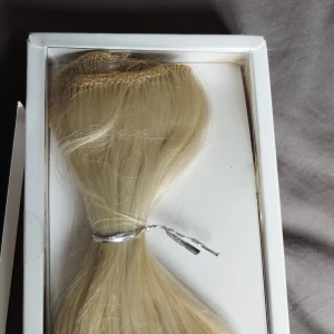 NY Blont syntetiskt löshår Rapunzel of Sweden  - Säljer ett nytt set blont syntetiskt löshår från Rapunzel of Sweden, 50cm, 90g. Det har en beach wave och ger extra längd och volym. Perfekt för att skapa en fylligare frisyr på bara några minuter. Oanvänd ny i box, men en liten slinga saknas, så det är fyra stycken istället för fem.