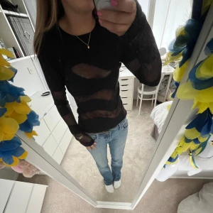 Svart meshtröja med transparenta partier - Säljer en svart långärmad meshtröja med transparenta vågformade partier. Tröjan är tight och har rund halsringning. Perfekt för dig som vill ha en edgy och trendig look.