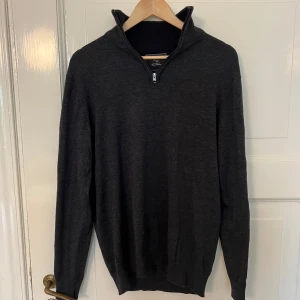 Stickad tröja med dragkedja från Carl William - Mörkgrå stickad tröja från Carl William i storlek M. Tröjan har halv dragkedja vid halsen. Perfekt för lager-på-lager och enkel att matcha med olika outfits.